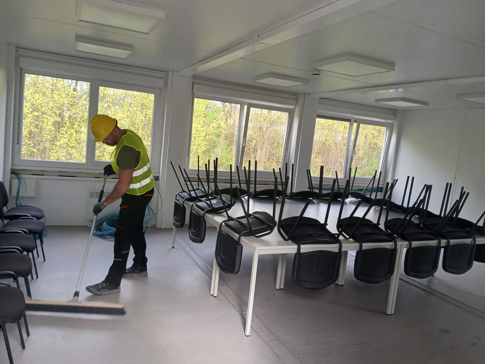 Mitarbeiter kehrt den Boden eines Bürocontainers